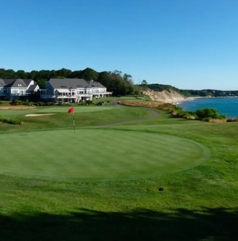 Flag on a green with clubhouse and bay behind